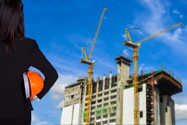 Mulher engenheira de pé no fundo da construção e segurando um capacete — Fotografia de Stock