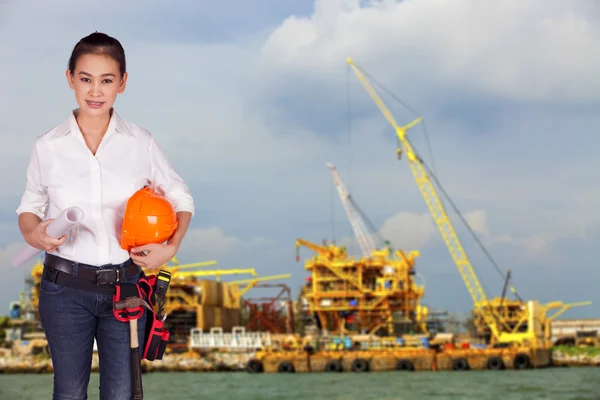 Woman engineer standing on the building background holding a hard hat and building plan — Stock Photo, Image