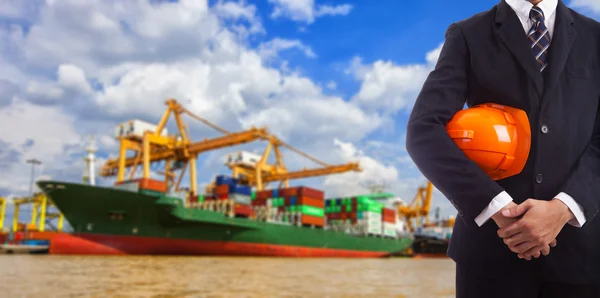 Affärsman som håller en röd hjälm på bakgrund av hamnen — Stockfoto