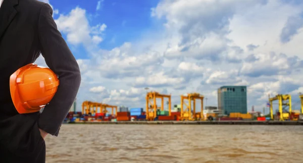 Businessman holding a red helmet on the background of the port — Stock Photo, Image