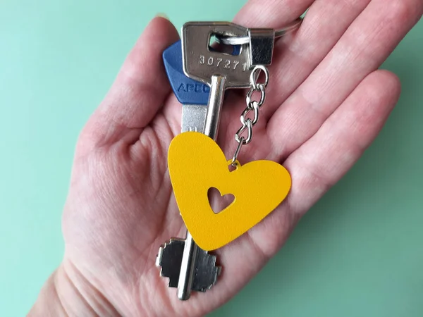 Sarı kalp anahtarlığını tutan el.
