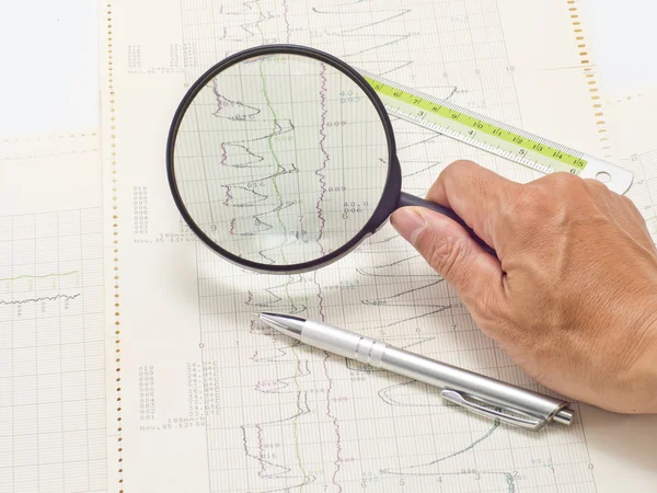 Glass on hand magnifying scientific graph to analysis the result — Stock Photo, Image