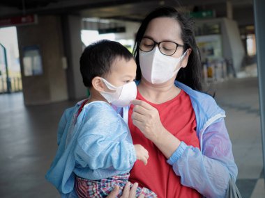 Coronavirus hastalığının resmi adı COVID-19 olan Coronavirus virüsünü önlemek için annesi ve Asyalı çocuk beyaz maske takıyor. .
