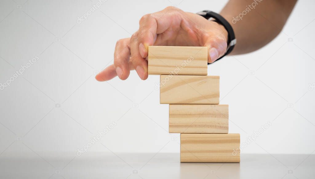 conceptual businessman fingers arranging  wooden blocks in the position among competition indicating his succesful and achievment by  strategy, planing and prevention.