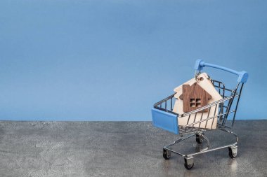 Alış veriş arabasındaki ahşap ev, arka plandaki gri duvarda mesaj için yer var. Bir ev alıyorum. İpotek ve kredi