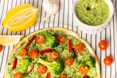 Brokolili vejetaryen pizza ve ıspanaklı pesto sosu, beyaz masada domatesler..