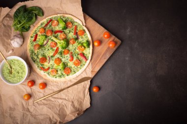 Brokolili vejetaryen pizza ve ıspanaklı pesto sosu, karanlık bir masada domates. Boşluğu kopyala