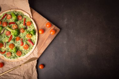 Lezzetli vejetaryen pizza. Brokolili vejetaryen pizza ve ıspanaklı pesto sosu, karanlık bir masada domates..