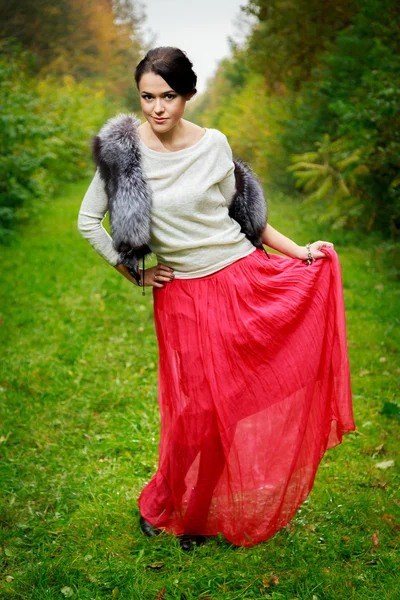 Belle fille dans une jupe rouge et un gilet de fourrure dans la forêt — Photo