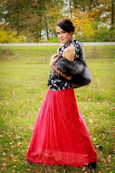 Hermosa chica en una falda roja y un chaleco de piel en el bosque — Foto de Stock