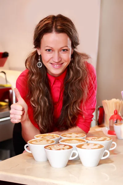 Žena s sedmi šálky cappuccina, ukazující trumb gesto — Stock fotografie