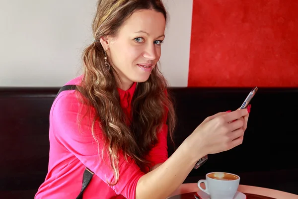 Dívka při pohledu na telefon a pít cappuccino — Stock fotografie