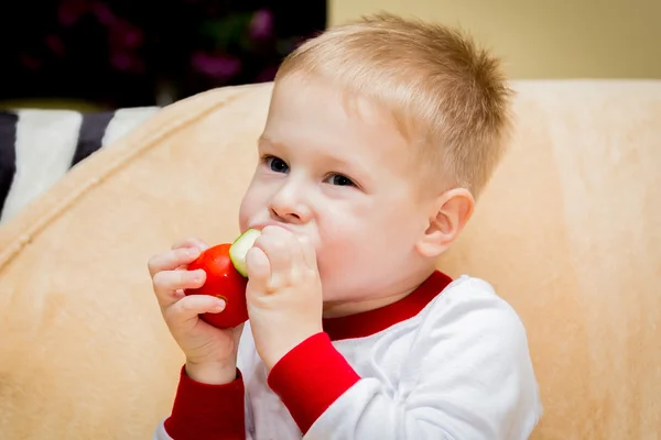 Kleine jongen eet een tomaat en komkommer — Stockfoto