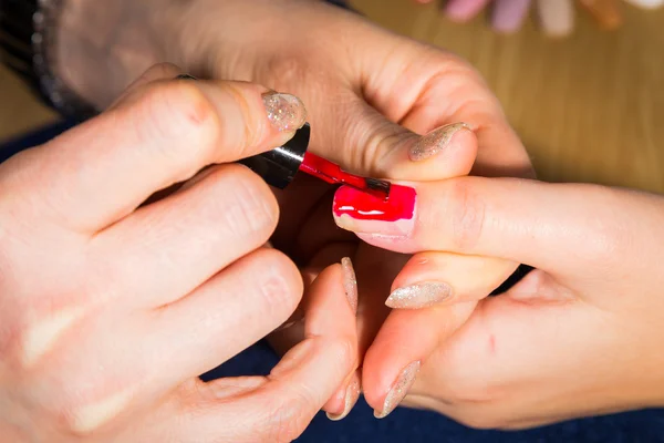 Esteticista aplicando verniz de unhas vermelhas nas unhas de um cliente — Fotografia de Stock