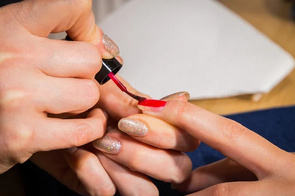 Esteticista aplicando esmalte rojo en las uñas de un cliente —  Fotos de Stock