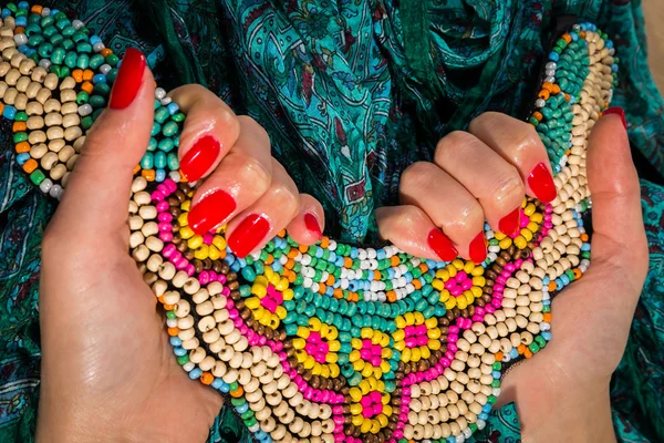 Female hands with red manicure holding colorful necklace — Stock Photo, Image