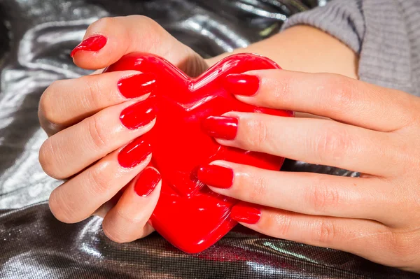 Mão com manicure vermelho segurando coração vermelho — Fotografia de Stock