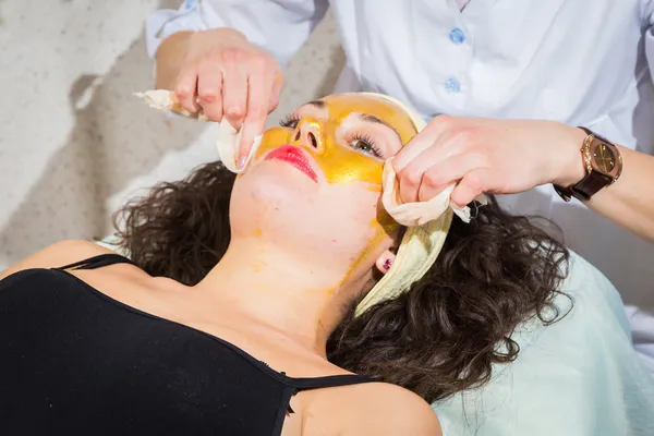 Cosmetologist doing gold facial mask  to face of woman