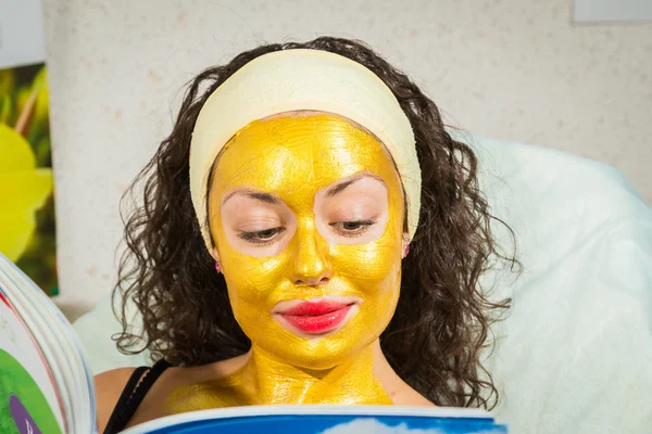 Mujer en oro máscara facial revista de lectura — Foto de Stock