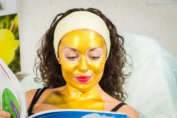 Woman in gold facial mask reading magazine