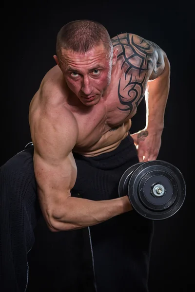 Musculoso hombre en tatuajes con mancuernas — Foto de Stock