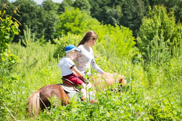 Niño montando pony con madre —  Fotos de Stock