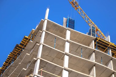 Yeni binanın şantiyesi. Endüstriyel yapı, beton duvarlar ve mavi gökyüzü arkaplan fotoğrafına karşı sarı vinç