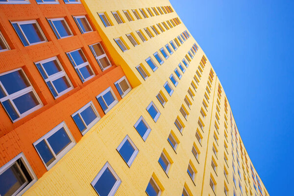 Modern multi-storey building with many glass windows standing against background of blue sky and sun. Residential buildings, urban real estate stock