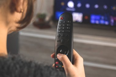 Kanepede TV karşısında uzaktan kumandalı bir kadın oturuyor ve yayın hizmetleri konseptini izliyor.
