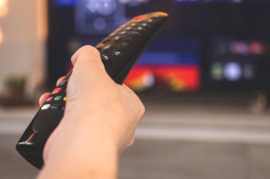 Uzaktan kumandalı kadın, televizyonun arka planı, modern oturma odasındaki yakın çekim fotoğrafı.