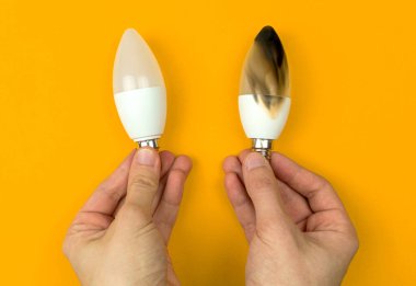 Yanmış LED ampulleri olan eller. Elektrik kısa devre kavramı. Evde yanan tel, tehlikeli, başarısız. Ev güvenliği. Üst manzara, sarı arkaplan 