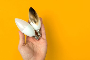 Yanmış LED ampulle el. Elektrik kısa devre kavramı. Evde yanan tel, tehlikeli, başarısız. Ev güvenliği. Üst manzara, turuncu arkaplan 