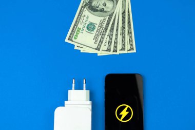Enerji verimliliği, enerji tasarrufu. Cep telefonu şarj aleti adaptörü ve para masanın üstünde. Flay lay lay, üst görünüm, mavi arkaplan fotoğrafı