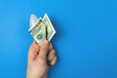 Gezegeni kurtar. Bir dolarlık banknotla LED ampulü elinde. Enerji ve ekonomi tasarrufu kavramı. Kopyalama alanı olan mavi arkaplan