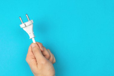 Elinde elektrik kablosu var. Parlak mavi arkaplan, düz konum, üst görünüm ve kopyalama alanı