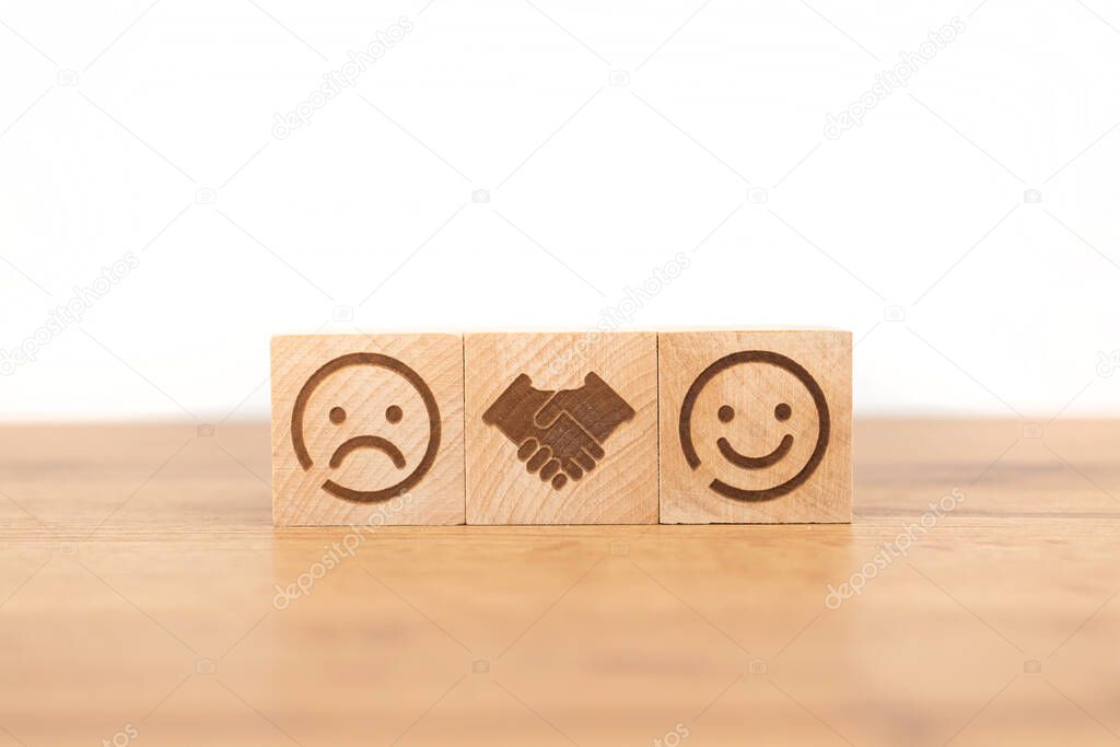 Customer satisfaction concept. Smiley and sad face icon on a wooden cube, hand shaking. Service rating, satisfaction and marketing 