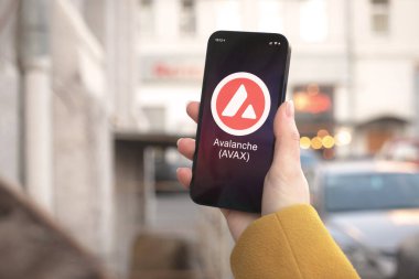Çığ AVAX kripto para birimi sembolü, logo. İş ve finansal konsept. Akıllı telefon ile el, kripto simgesi ile ekran kapatma