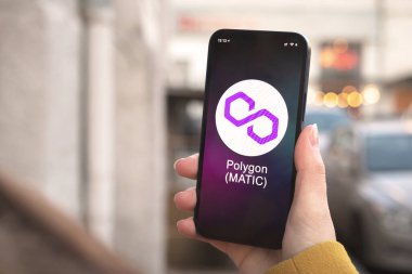 Çokgen MATIC kripto para birimi sembolü, logo. İş ve finansal konsept. Akıllı telefon ile el, kripto simgesi ile ekran kapatma