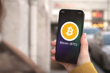 Bitcoin BTC şifreleme sembolü, logo. İş ve finansal konsept. Akıllı telefon ile el, kripto simgesi ile ekran kapatma