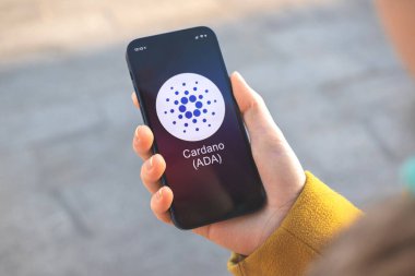 Cardano ADA kripto para birimi sembolü, logo. İş ve finansal konsept. Akıllı telefon ile el, kripto simgesi ile ekran kapatma