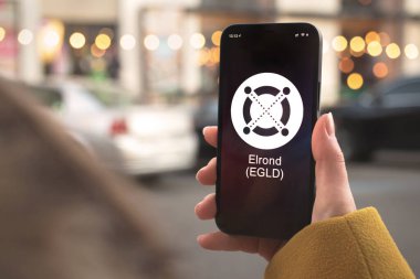 Elrond EGLD şifreleme sembolü, logo. İş ve finansal konsept. Akıllı telefon ile el, kripto simgesi ile ekran kapatma