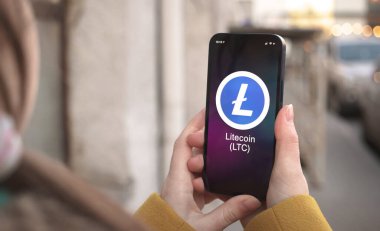 Litecoin LTC şifreleme sembolü, logo. İş ve finansal konsept. Akıllı telefon ile el, kripto simgesi ile ekran kapatma