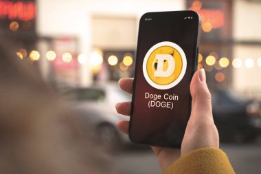 Dogecoin DOGE kripto para birimi sembolü, logo. İş ve finansal konsept. Akıllı telefon ile el, kripto simgesi ile ekran kapatma