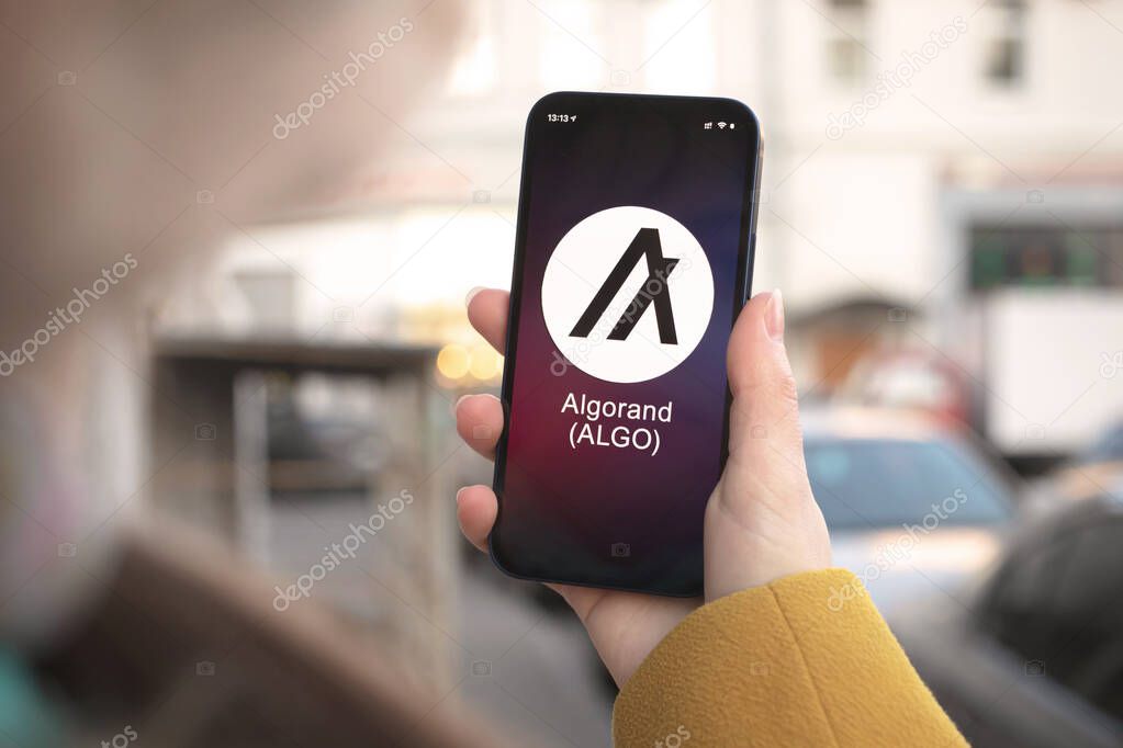 Algorand ALGO cryptocurrency symbol, logo. Business and financial concept. Hand with smartphone, screen with crypto icon closeup