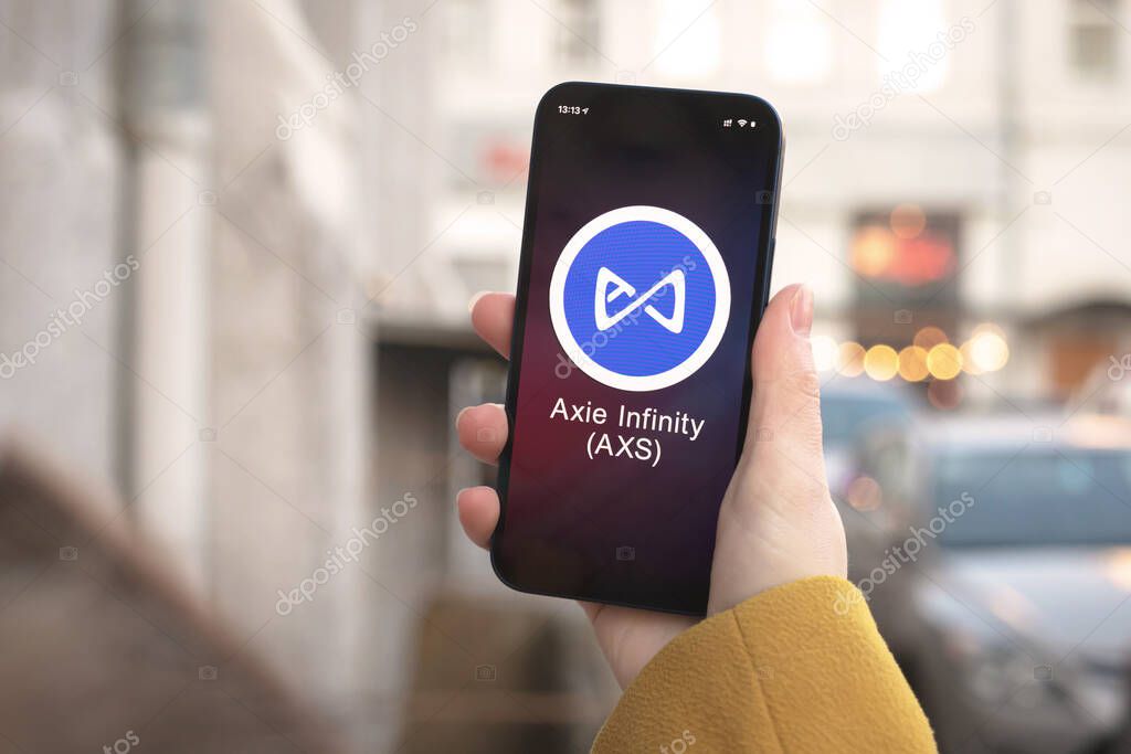 Axie Infinity AXS cryptocurrency symbol, logo. Business and financial concept. Hand with smartphone, screen with crypto icon closeup