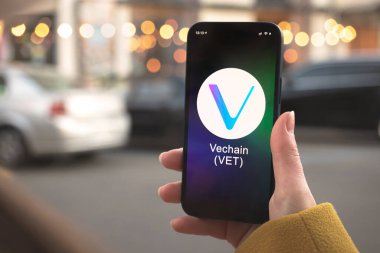 Vechain VET kripto para birimi sembolü, logo. İş ve finansal konsept. Akıllı telefon ile el, kripto simgesi ile ekran kapatma