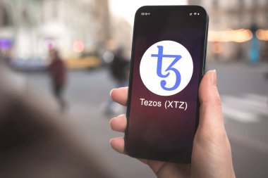 Tezos XTZ şifreleme sembolü, logo. İş ve finansal konsept. Akıllı telefon ile el, kripto simgesi ile ekran kapatma