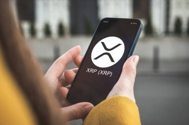 Dalgalanan XRP şifreleme sembolü, logo. İş ve finansal konsept. Akıllı telefon ile el, kripto simgesi ile ekran kapatma