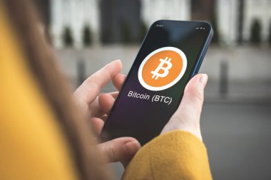 Bitcoin BTC şifreleme sembolü, logo. İş ve finansal konsept. Akıllı telefon ile el, kripto simgesi ile ekran kapatma
