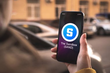 Sandbox şifreleme sembolü, SAND logosu. İş ve finansal konsept. Akıllı telefon ile el, kripto simgesi ile ekran kapatma